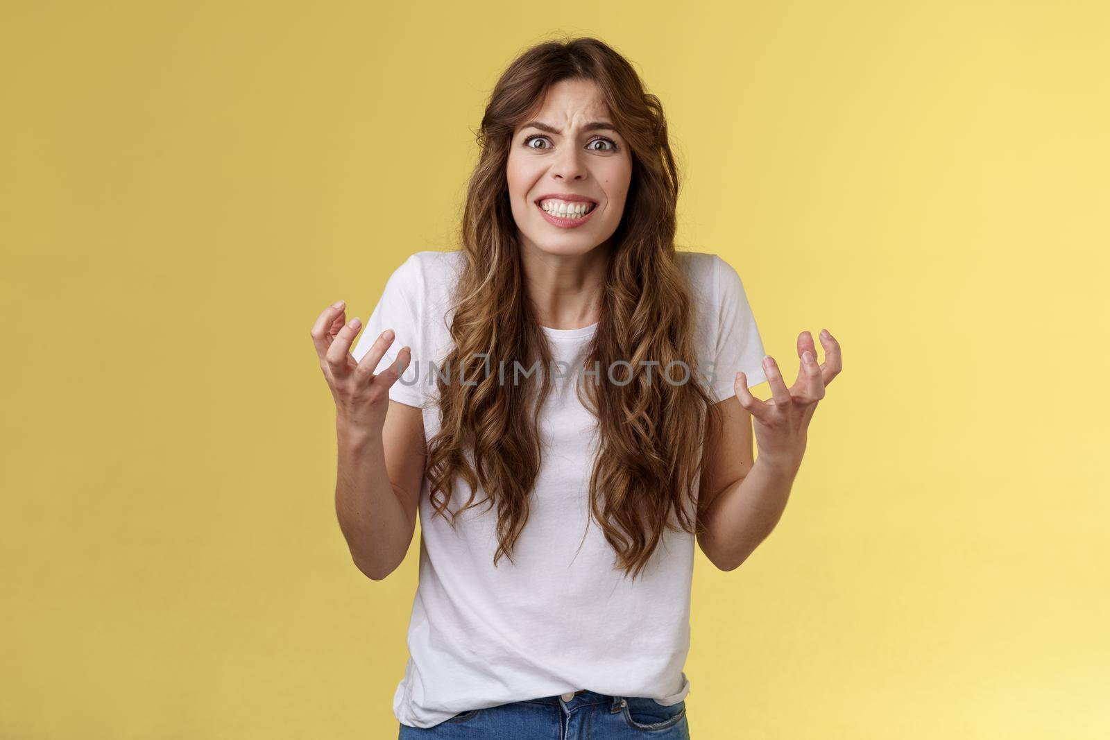 Annoyed curly-haired caucasian irritated distressed girl cringe outraged clench teeth frowning furious sqeez fists hateful complaining arguing pressured upset fighting have quarrel yellow background.