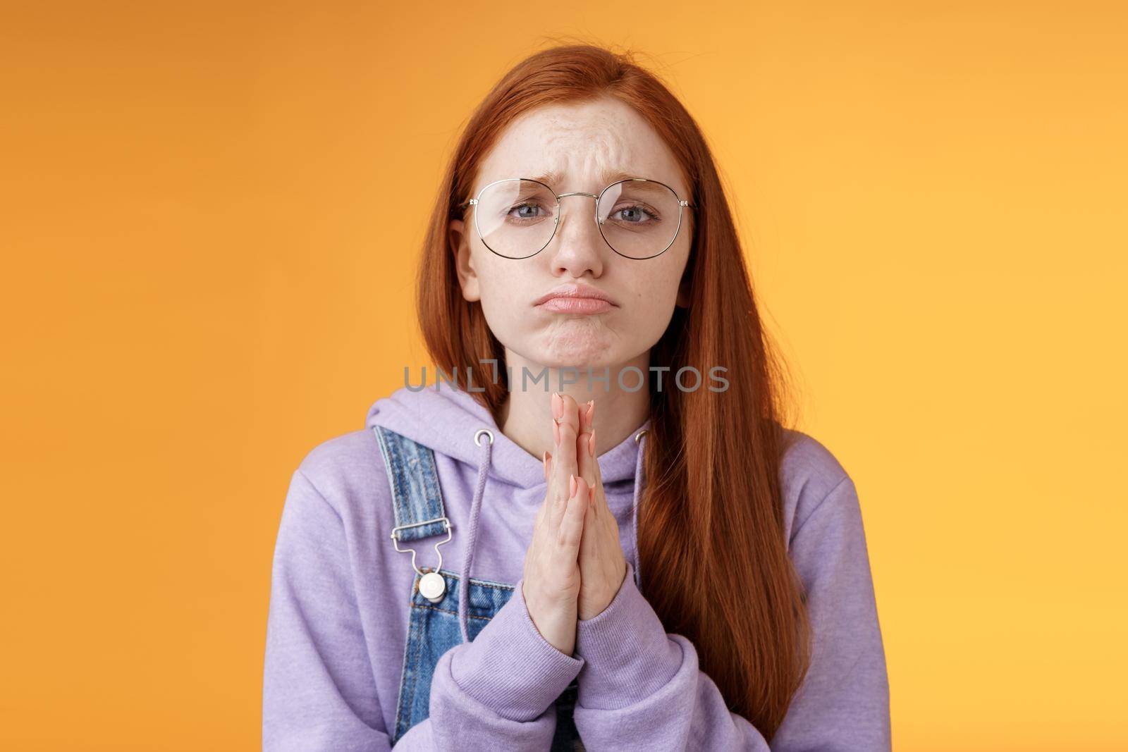 Please beg you. Clingy upset sad caucasian redhead girlfriend wearing glasses frowning grimacing pouting pleading help asking favour need urgently borrow something, orange background by Benzoix
