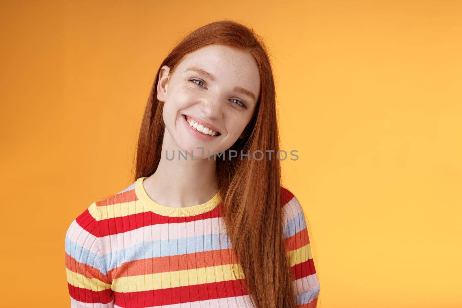 Pleasant charismatic young confident carefree redhead charming girl tilting head smiling broadly white teeth talking casually good mood express positive happy emotions standing orange background.