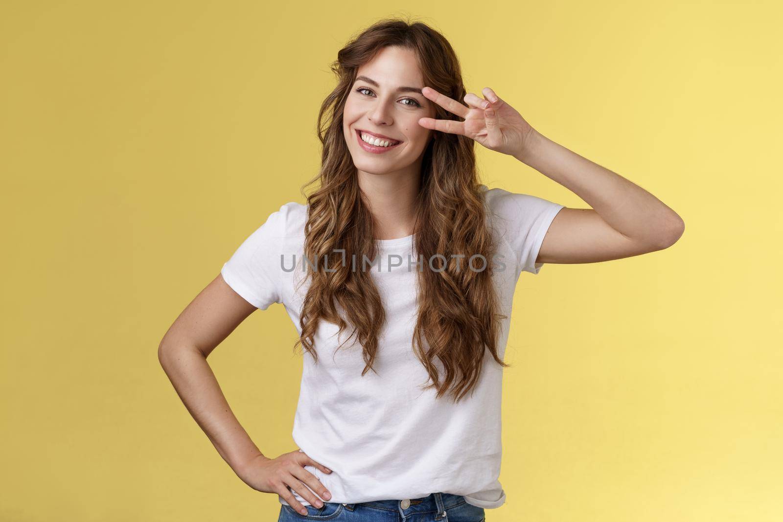 Positive outgoing enthusiastic good-looking woman having fun enjoy weekend summer vacation travel show peace sign victory gesture on eye tilt head having fun smiling broadly yellow background. Lifestyle.