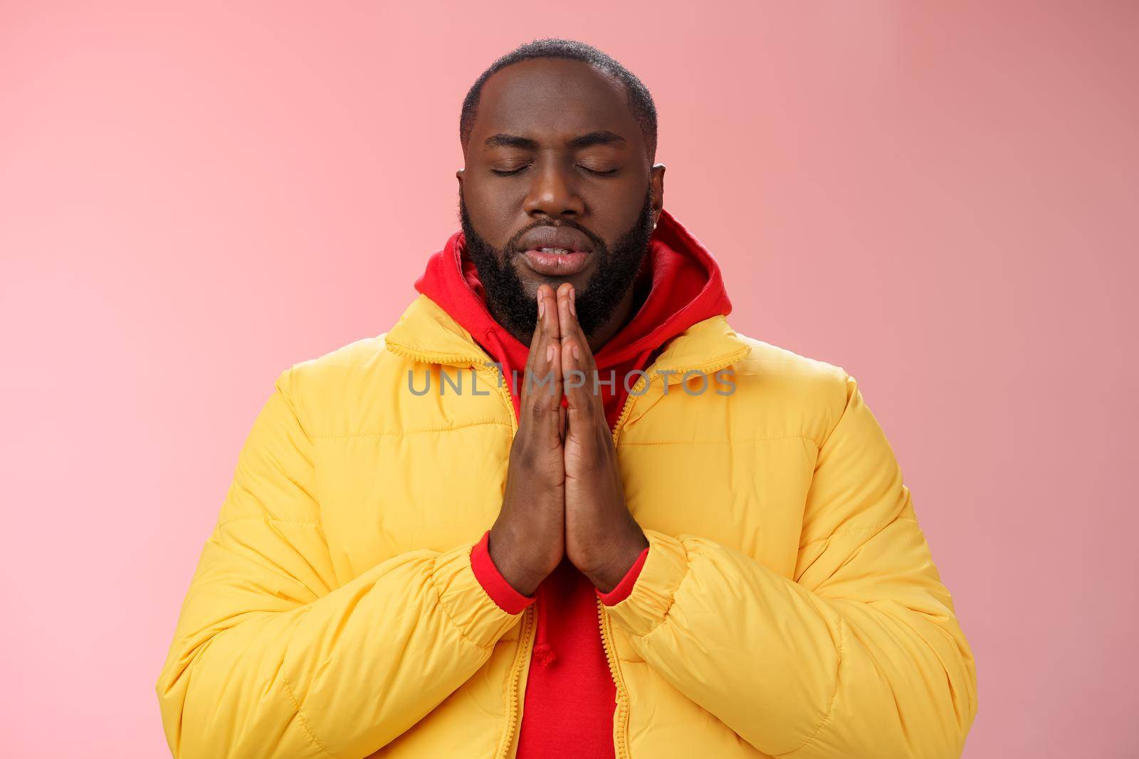 Serious-looking faithful young determined african-american praying guy in yellow coat press palms together pray close eyes whisper supplication asking god help make wish, standing pink background by Benzoix