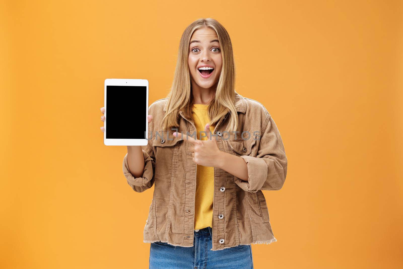 Woman showing friends new digital tablet first purchace of autumn. Charismatic and enthusiastic excited caucasian female with tanned skin and fair hair in corduroy jacket pointing at gadget screen. Emotions and technology concept
