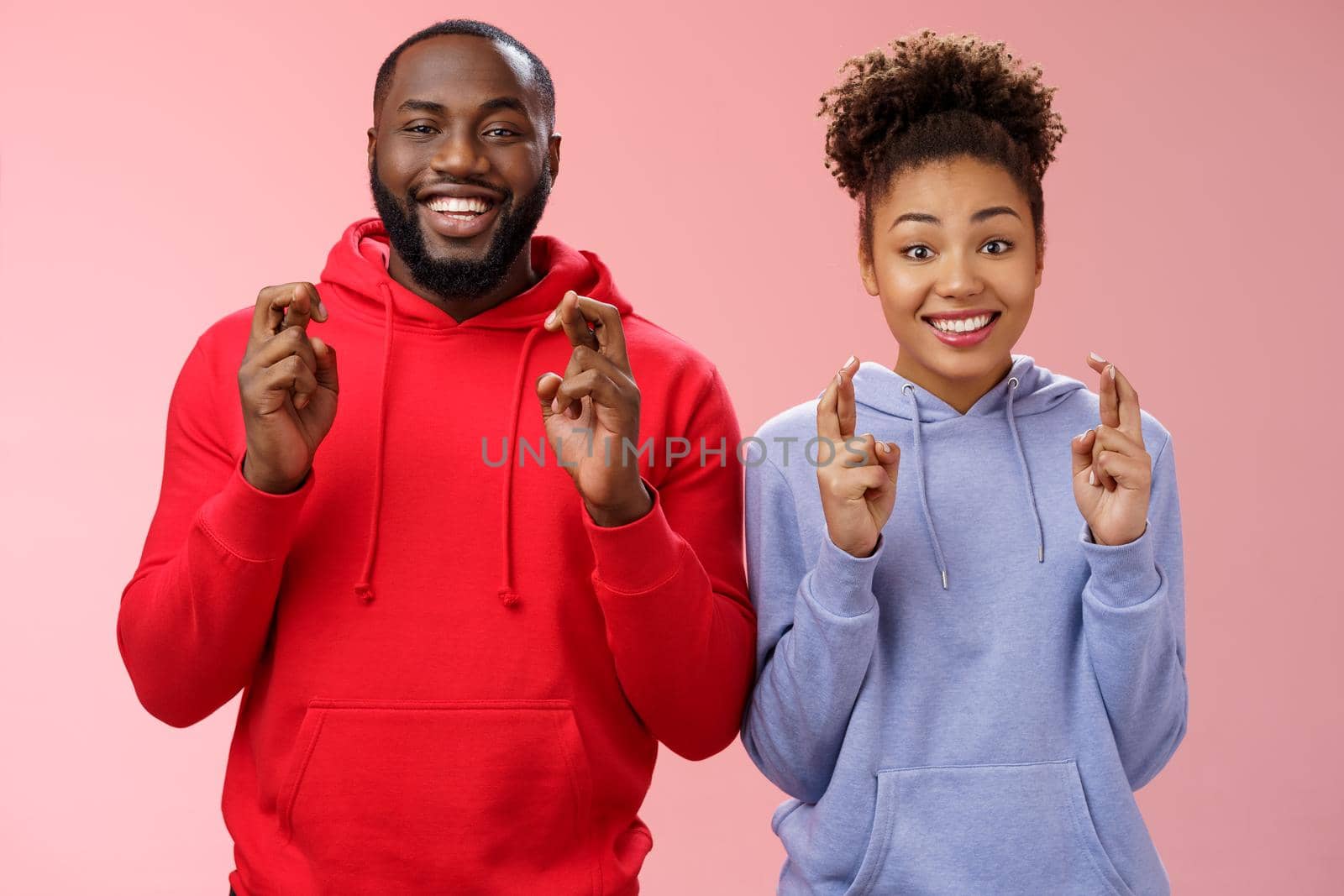 Lucky charming attractive positive african-american friends guy girl cross fingers making wish smiling broadly excited believe faithfully dream come true hopefully look camera, anticipating miracle.
