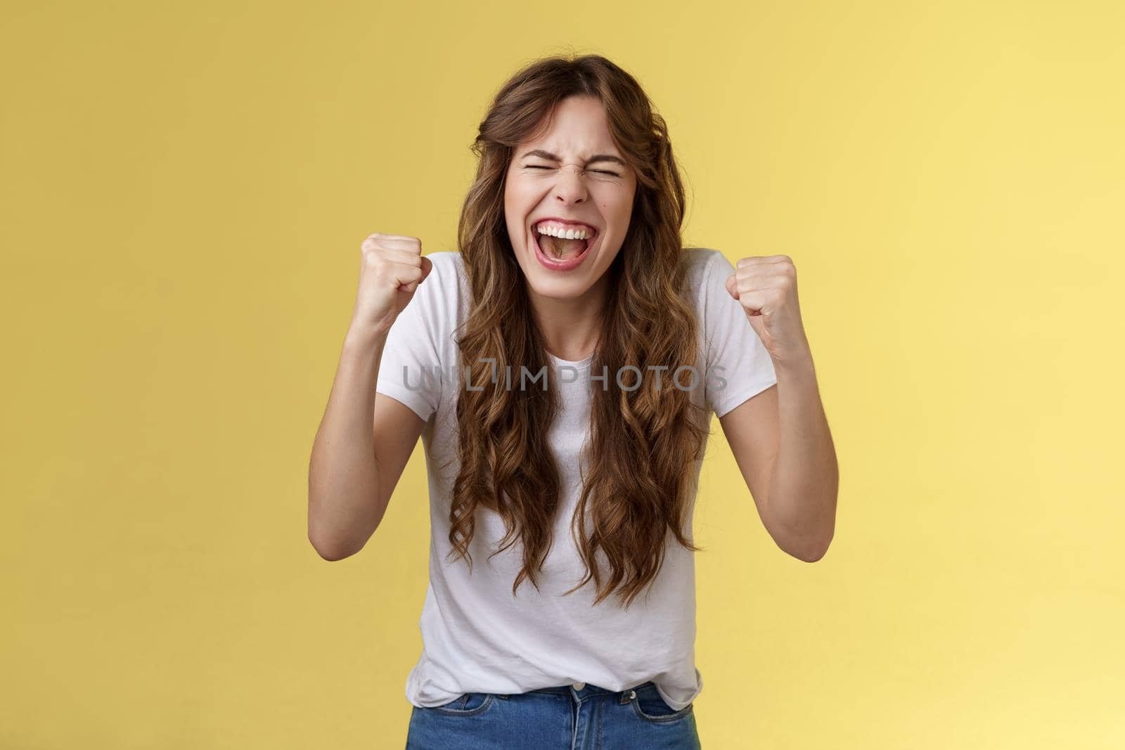 Cheerful excited happy enthusiastic girl yelling rooting wanna win badly fist pump celebratory satisfied awesome success winning triumphing joyfully close eyes shaking clench arms yellow background. Lifestyle.