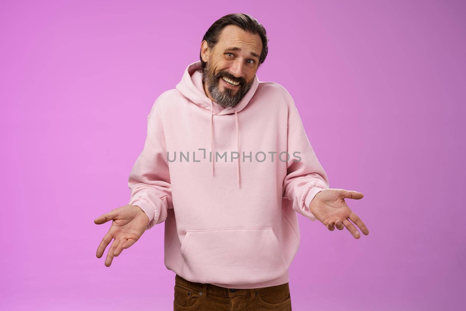 Portrait doubtful unsure awkward mature man shrugging spread hands sideways clueless cringing frowning hesitant cannot say yes no facing hard decision standing perplexed purple background.
