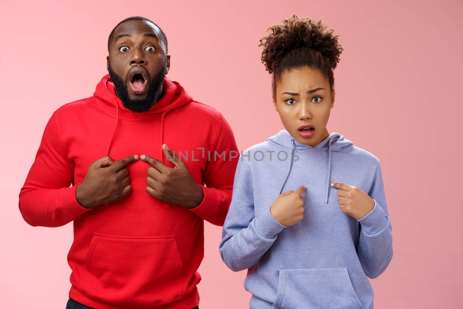 Why us. Shocked disturbed complaining two african american brother sister pointing chest index fingers frowning bothered upset man widen eyes surprised woman frowning sorrow, standing pink wall.