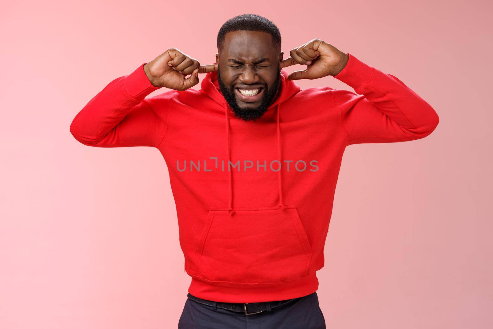 Annoyed bothered uncomfortable young african-american pressured and stressed bearded guy clench teeth cringing grimacing fed up irritated hearing loud noise bothering sound close ears by Benzoix