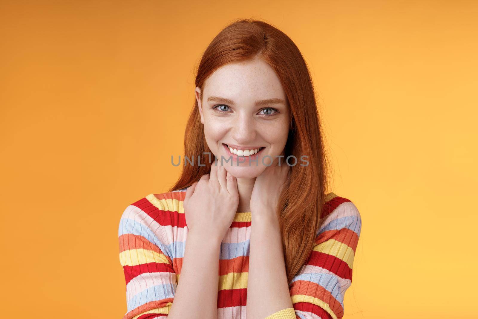 Pleased happy tender feminine redhead gorgeous girl blushing flirty giggle gazing camera smiling broadly touching neck modesy shy sensually talking guy likes standing orange background silly. Lifestyle.