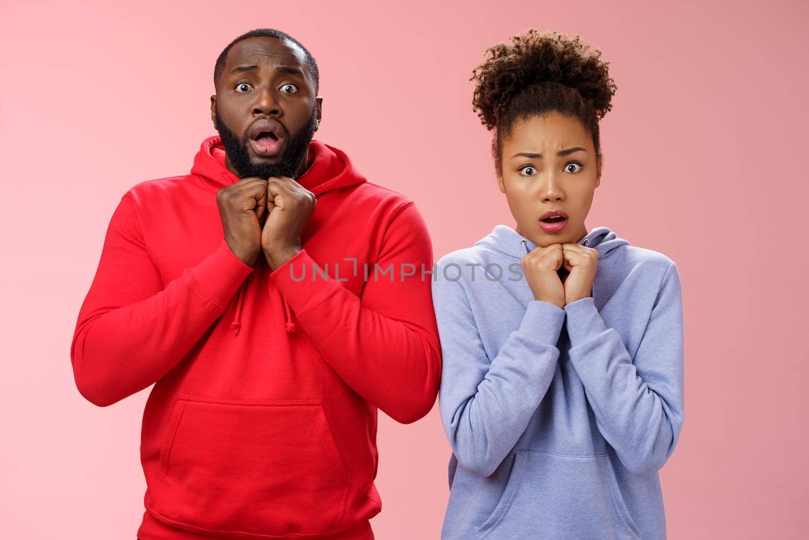 Upset worried two siblings watching together scary disturbing horror movie gasping frowning cringing shock intense emotions press hands chest widen eyes terrified standing nervous pink background.