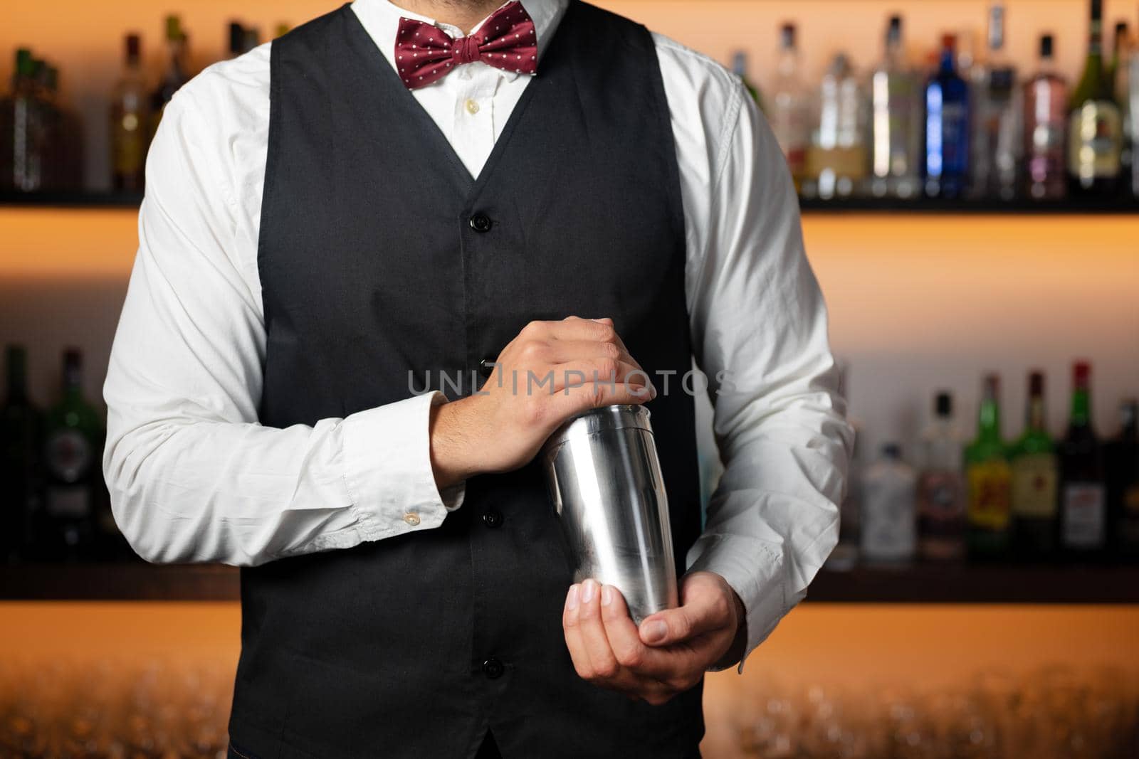 Cool professional bartender making a cocktail, shaking a cocktail shaker. Authentic barman making alcohol beverages in modern bar. by HERRAEZ