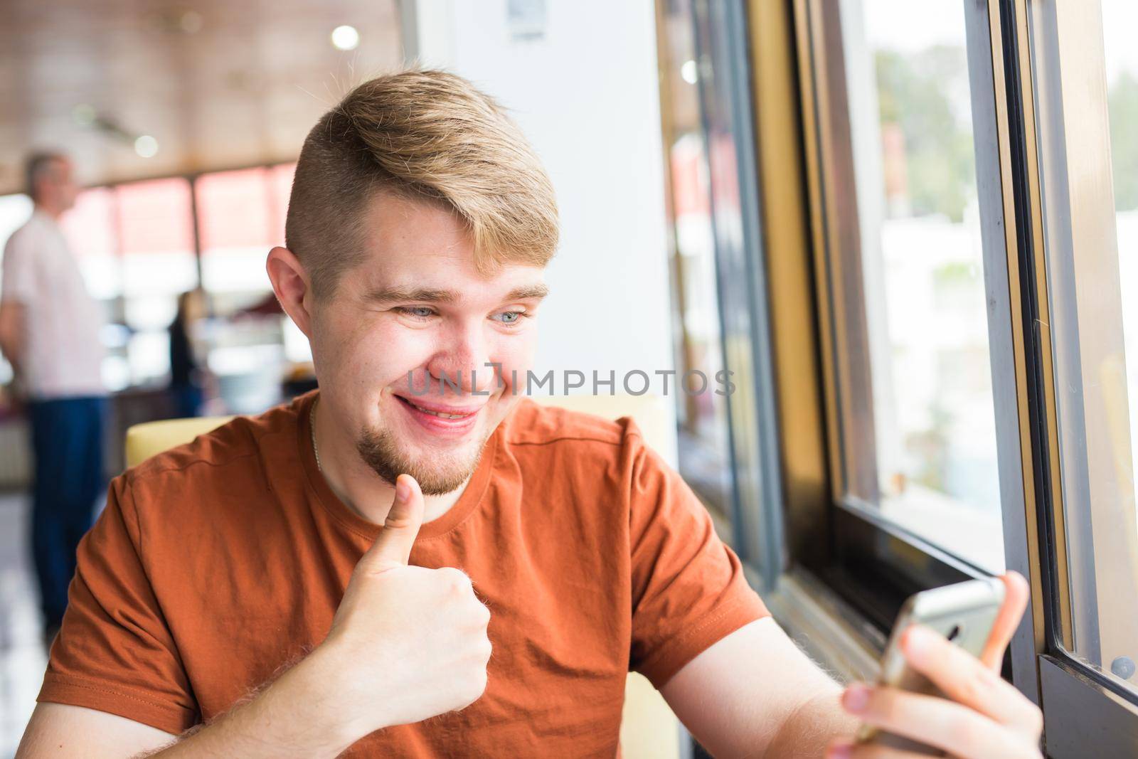 technology, communication and people concept - Young man holding a smart phone with thumbs up.