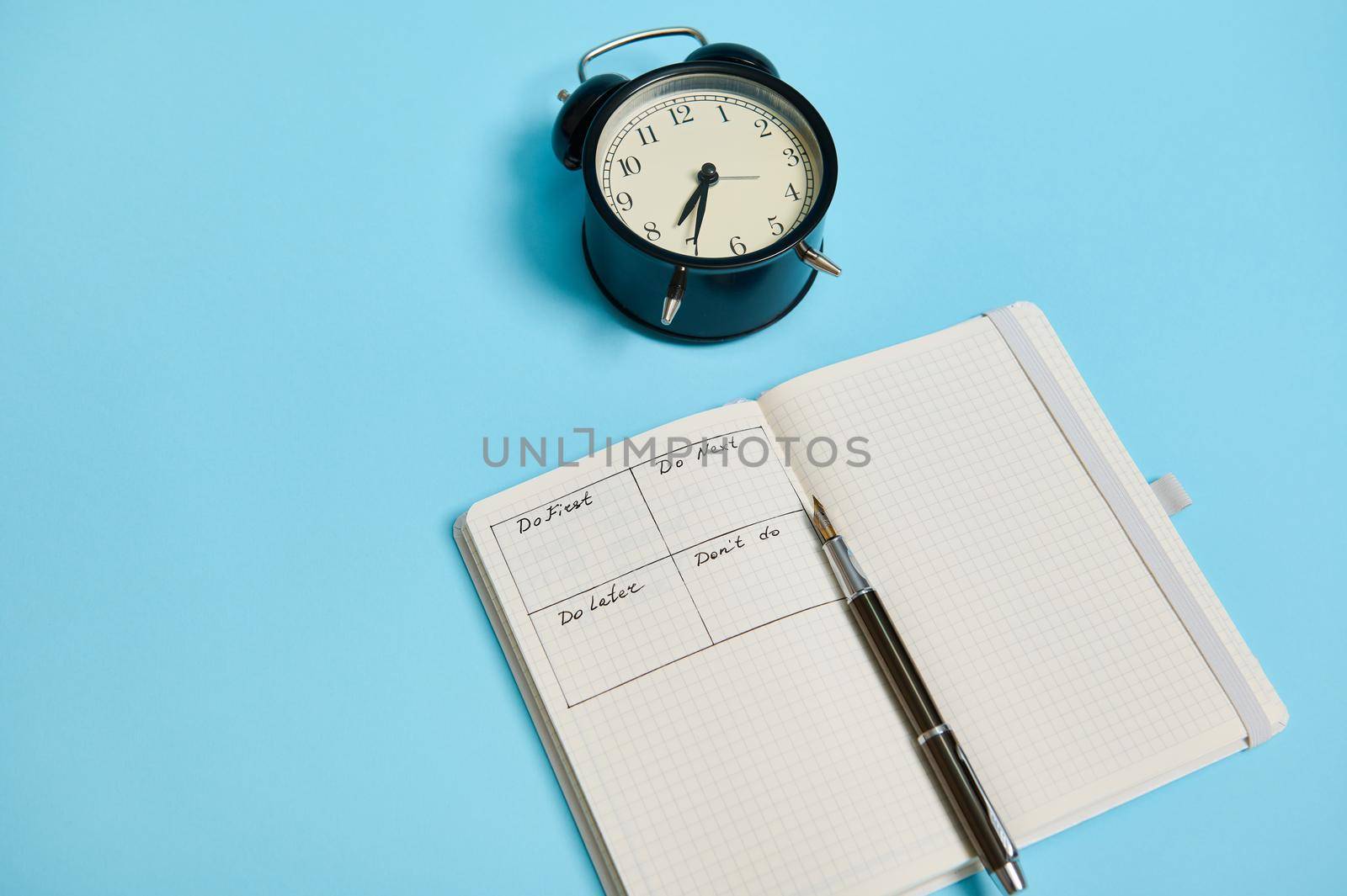 An open organizer notebook with timetable of the day by hour, pen, alarm clock on colored background with copy space. Time management, deadline and concept of proper planning and organization of time