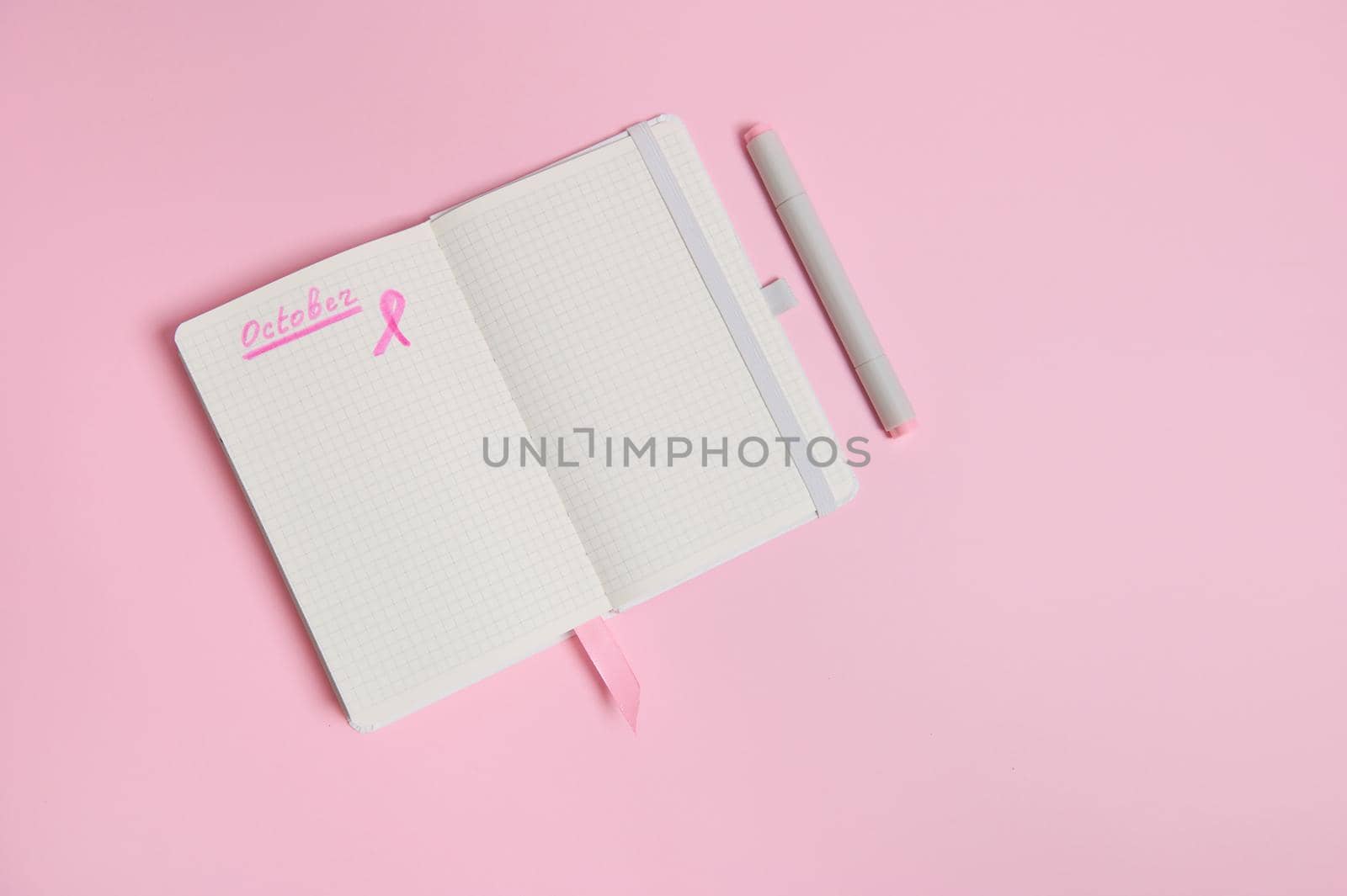 Lettering 1 st October on a diary and a pink ribbon on an empty blank paper sheet, isolated on pink background with copy space. World Breast Cancer Day