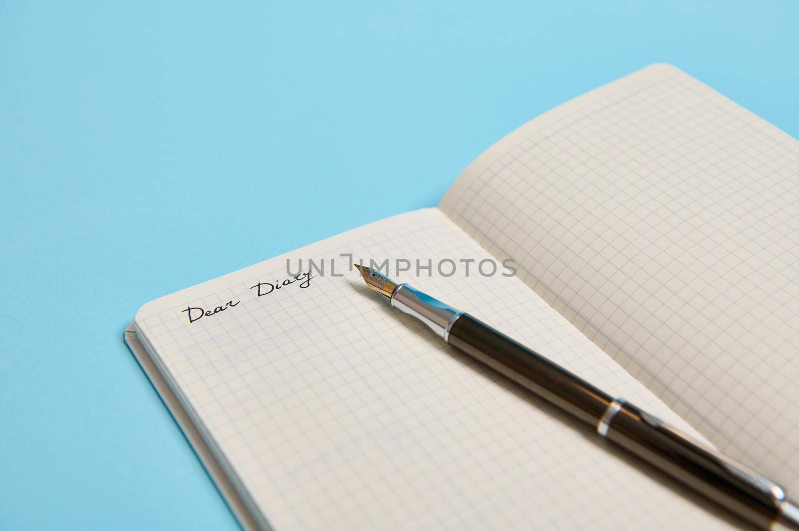 Cropped studio shot of an open notepad with word Dear Diary and an ink pen isolated on blue background with copy space for text