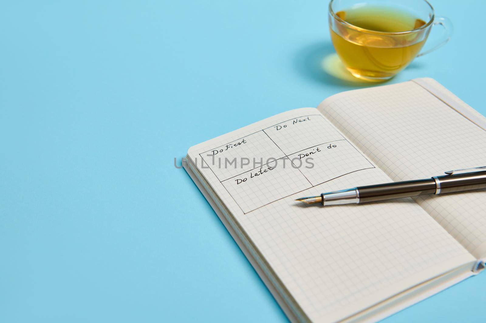 Time management, deadline concept: Cropped image of an open organizer notebook with timetable of the day by hour, ink pen, cup of tea on color background, copy space.