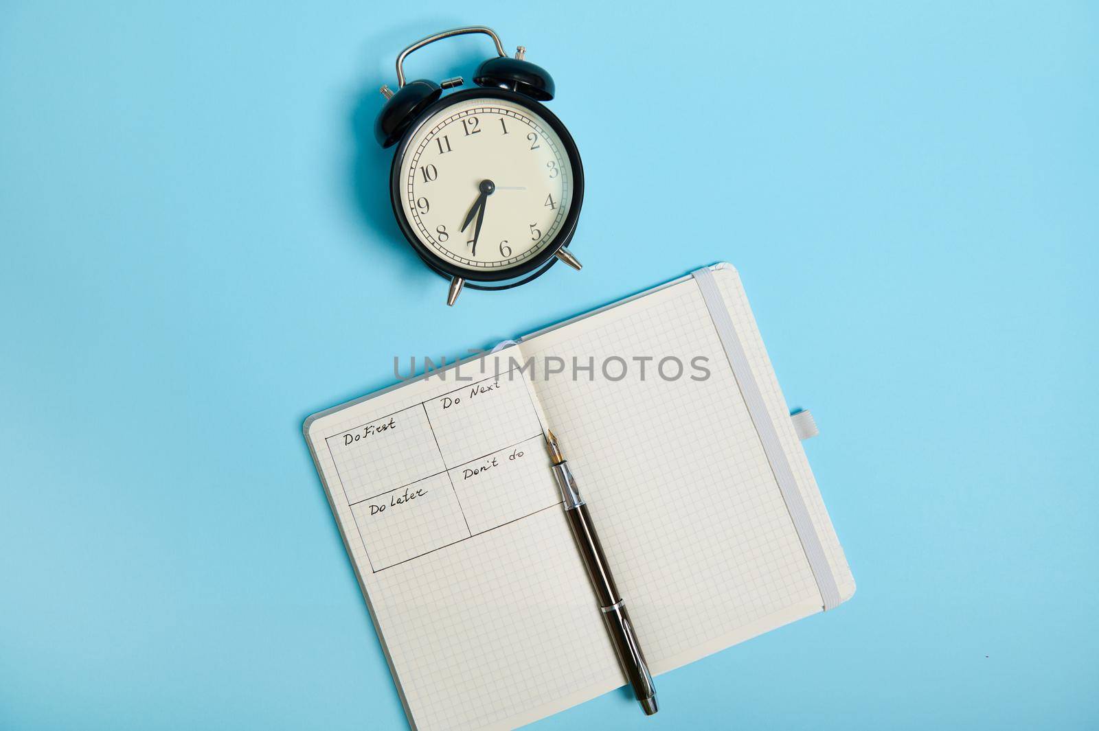 Flat lay of open notebook with timetable of the day by hour, pen, alarm clock on colored background with copy space. Time management, deadline and concept of proper planning and organization of time.