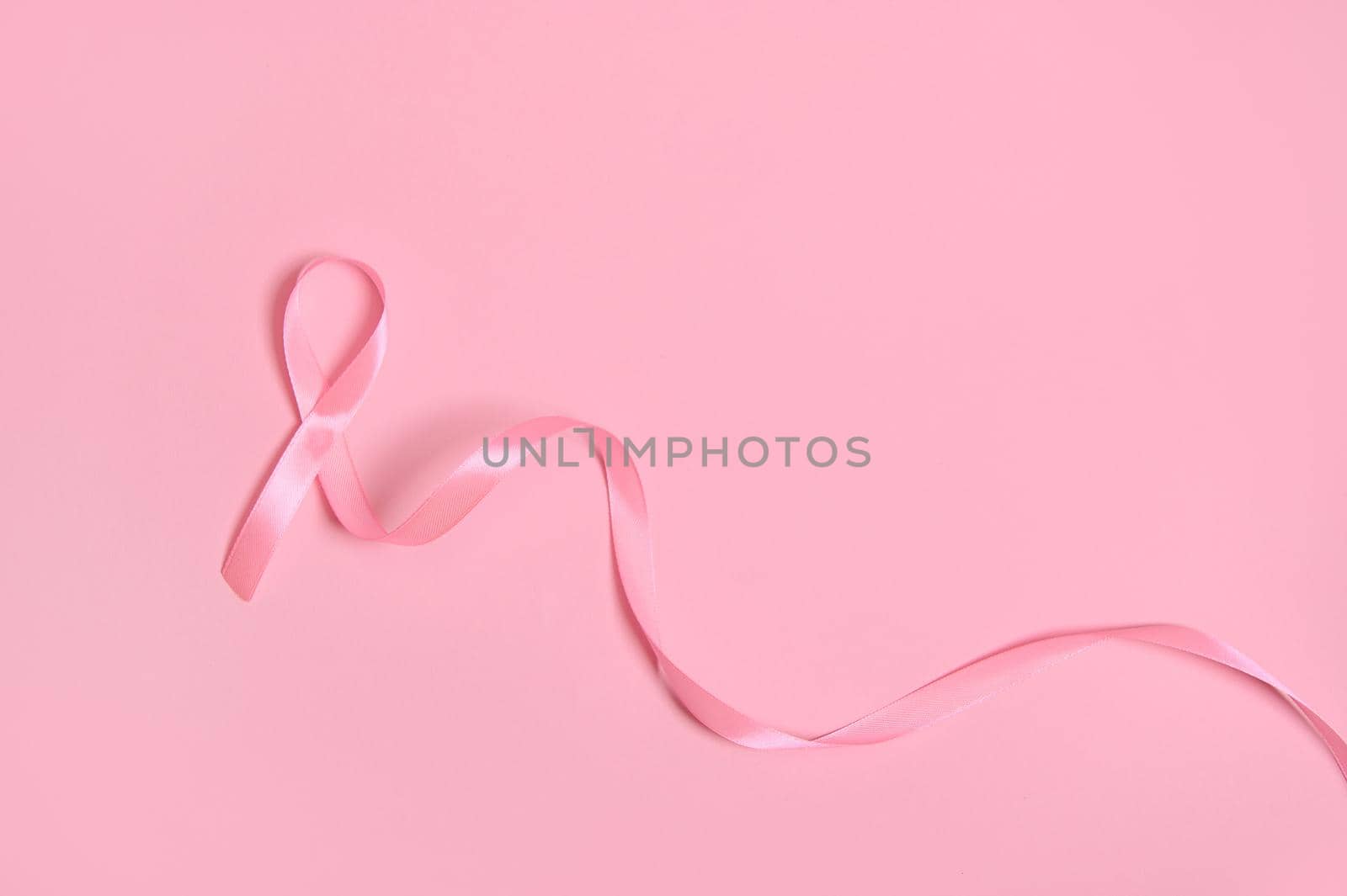 Top view of a long pink satin ribbon, where one end is endless. Breast Cancer Awareness, medical concept isolated on pink background with copy space. October awareness month campaign.