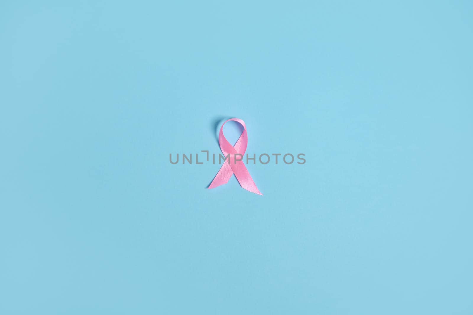 Flat lay of a satin pink ribbon awareness, International symbol of Breast Cancer Awareness Month in October. Isolated over on blue background with copy space . Medical and Women's health care concept. by artgf