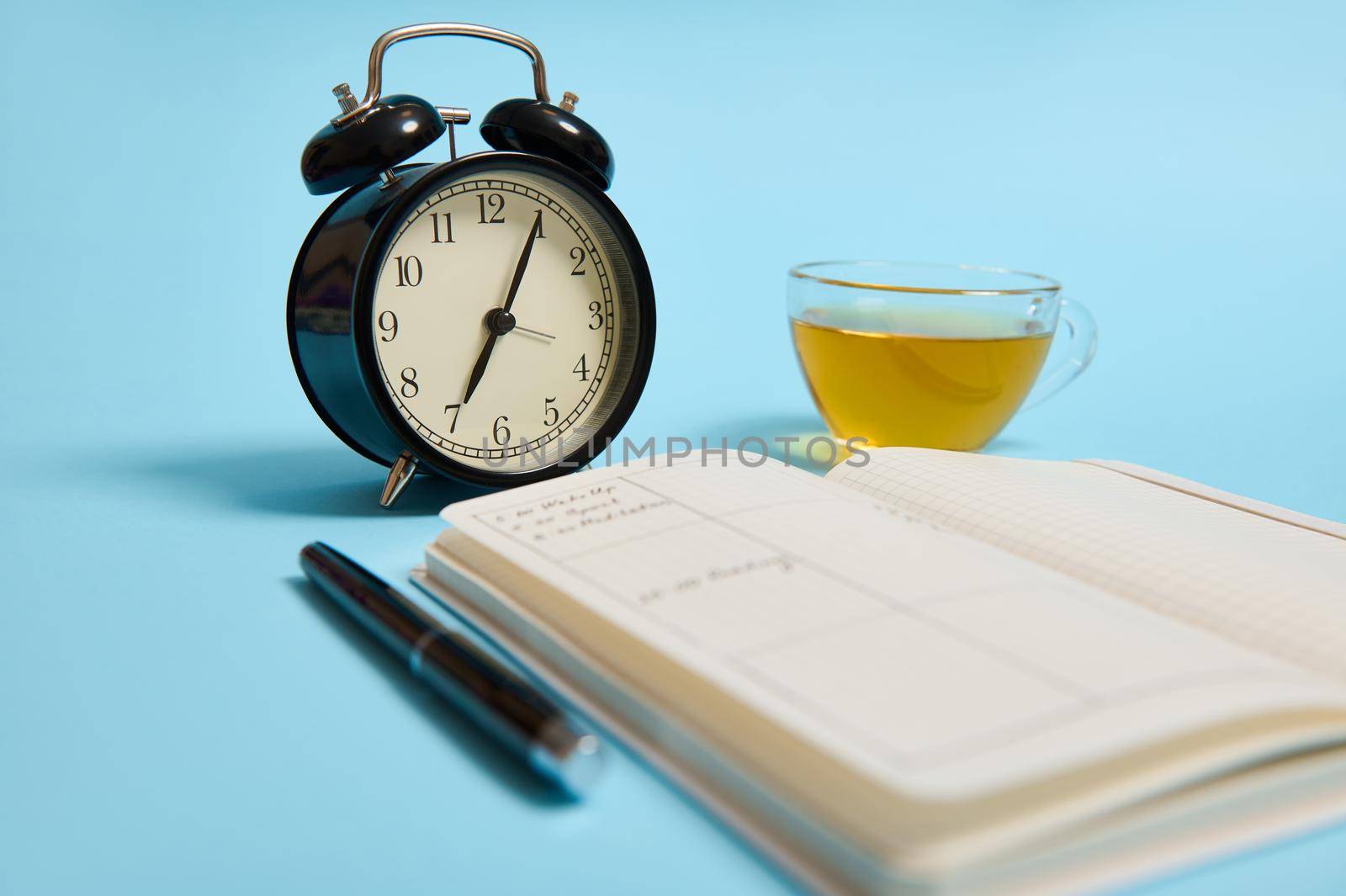 An open notebook with schedule, ink pen, black alarm clock lie on blue surface. Color background with copy space. Time management, deadline and schedule concept by artgf