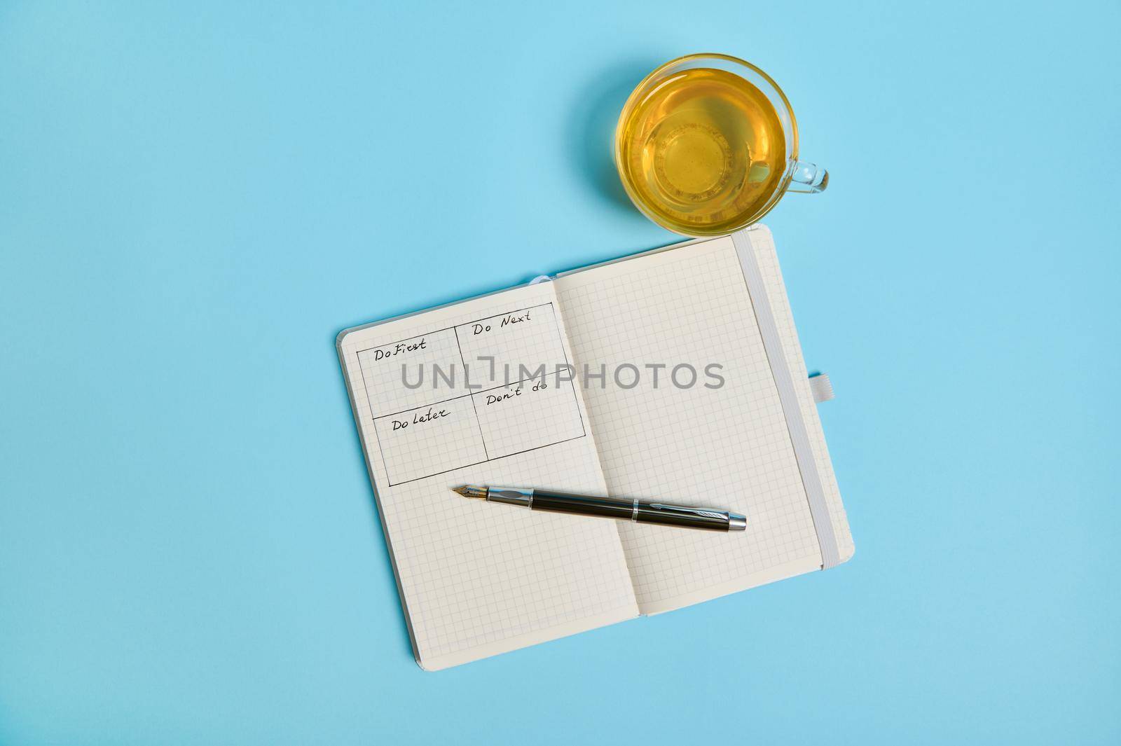 Time management, deadline concept: Flat lay of an open organizer notebook with timetable of the day by hour, ink pen, a tea cup on color background, copy space. Cropped image by artgf