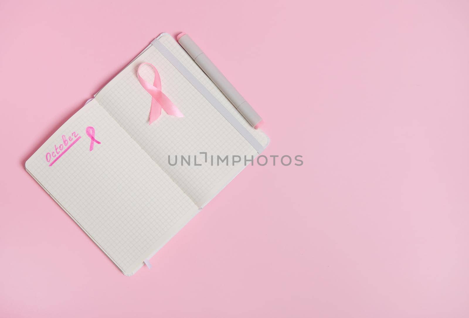 Lettering 1 st October on a diary and a pink ribbon on an empty blank paper sheet, isolated on pink background with copy space. October Pink day, World Cancer Day, national Cancer Survivor Say.