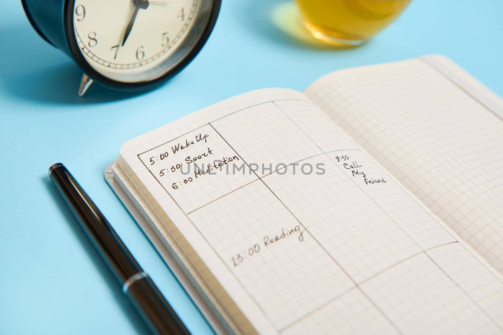 Cropped image of an open notebook with schedule, ink pen, black alarm clock lie on blue surface. Color background with copy space for text . Time management, deadline and schedule concept