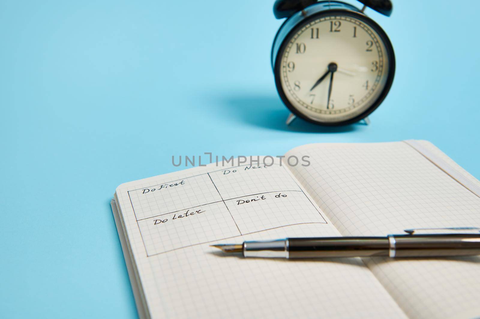 Time management, deadline concept: Cropped image of an open organizer notebook with timetable of the day by hour, ink pen, alarm clock on color background, copy space.