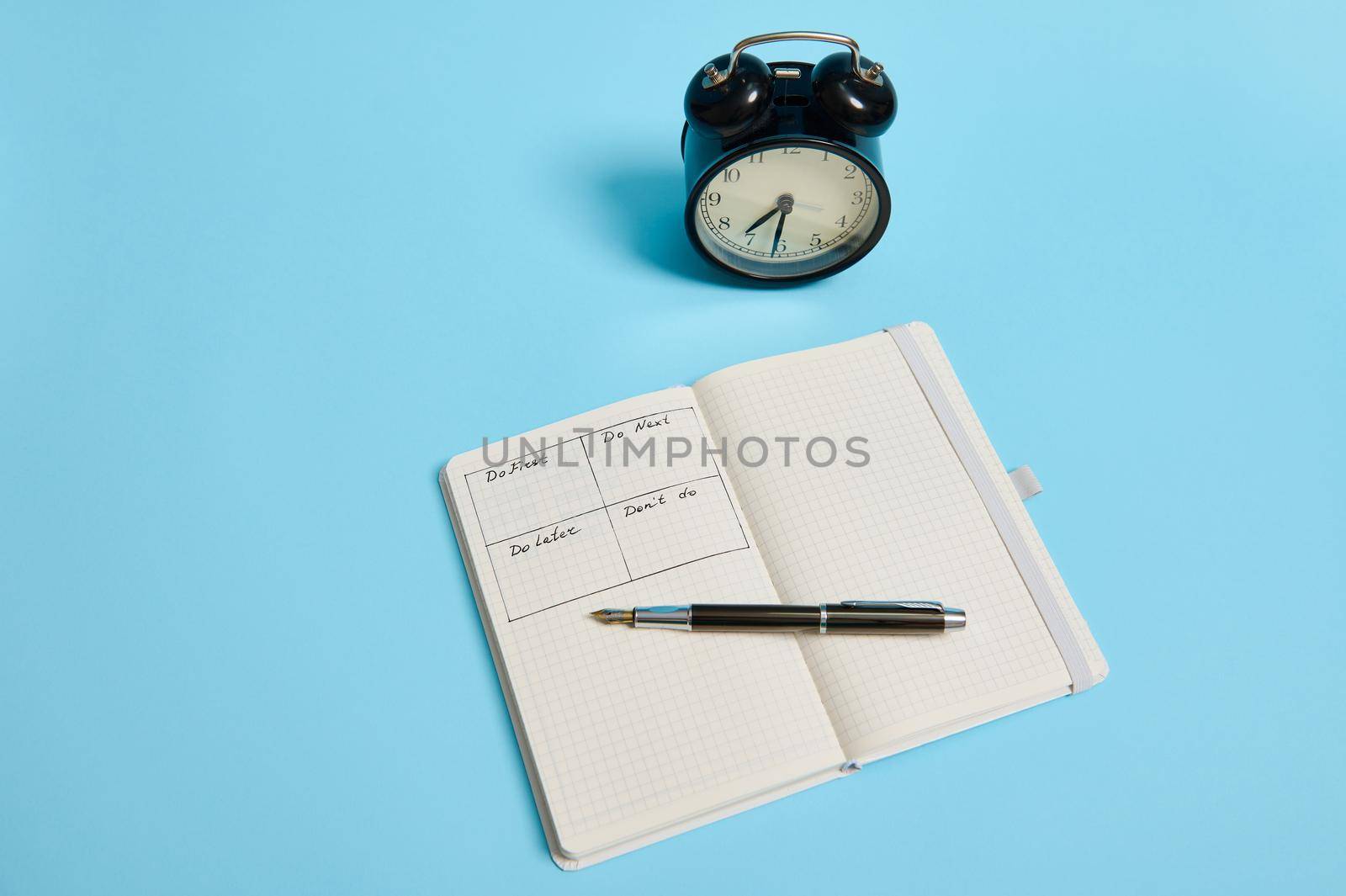 Time management, deadline and concept of proper planning and organization of time: An open organizer notebook with timetable of the day by hour, ink pen, alarm clock on color background, copy space.