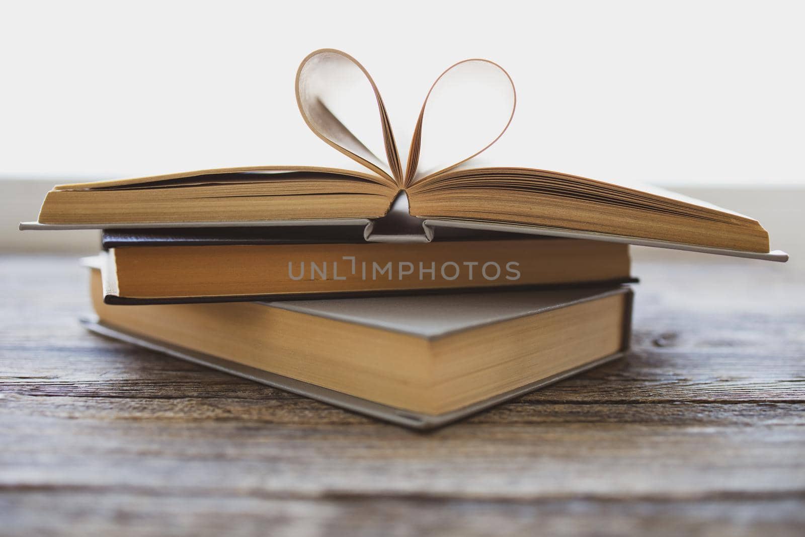 Composition of love with open book heart. Old books on a wooden table. Pages of the book in the form of heart. Heart shape for love in valentine day with blurred background. Vintage color tone style.