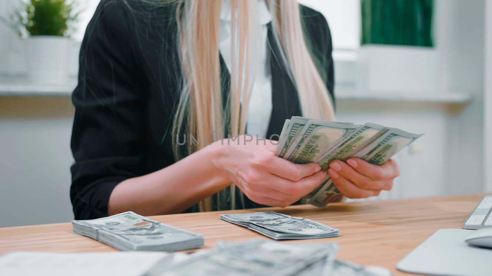 Business woman counting cash in hands. Crop view of female in elegant suit sitting at wooden desk and counting large bundle of dollar banknotes in hands. by art24pro
