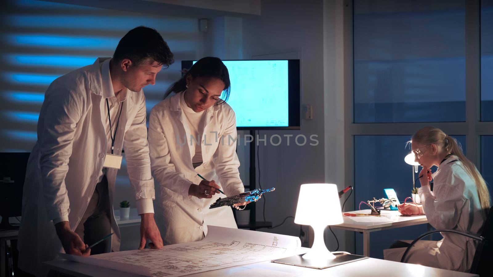 Man and woman in lab coats working in electronics lab with motherboard and control electronics scheme by art24pro