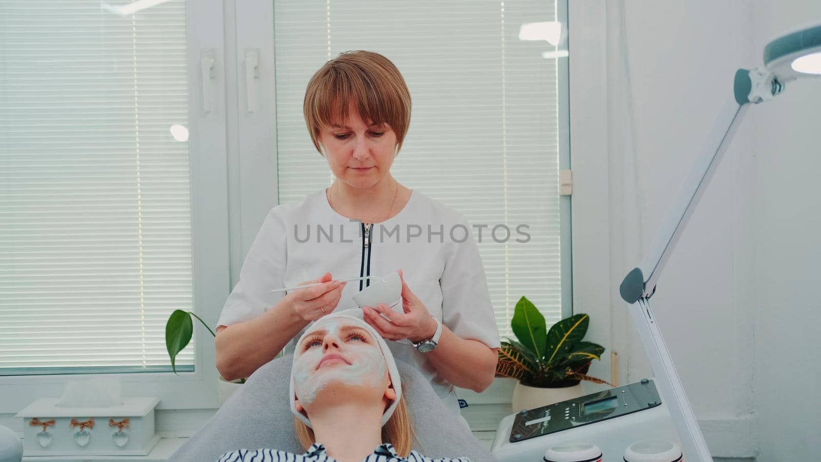 Beautician putting cream mask on woman's face at beauty salon by art24pro