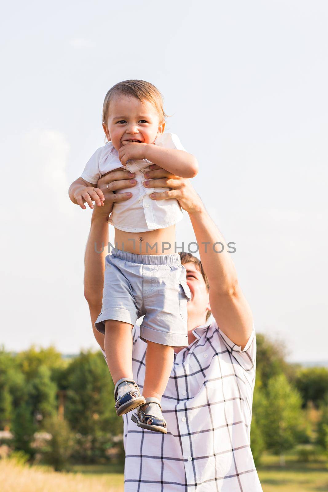 Happy young father and son playing together and having fun in the summer or autumn field. Family, child, fatherhood and nature concept.
