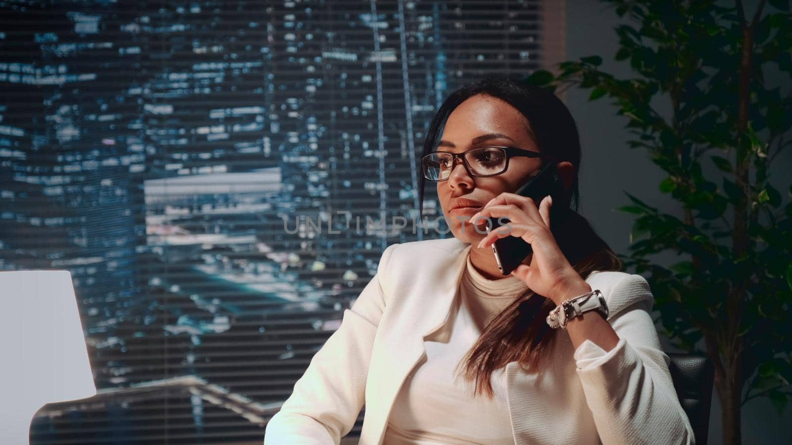 Close up of multiracial business lady speaking by smartphone with a client at her office. She is in black eyeglasses.