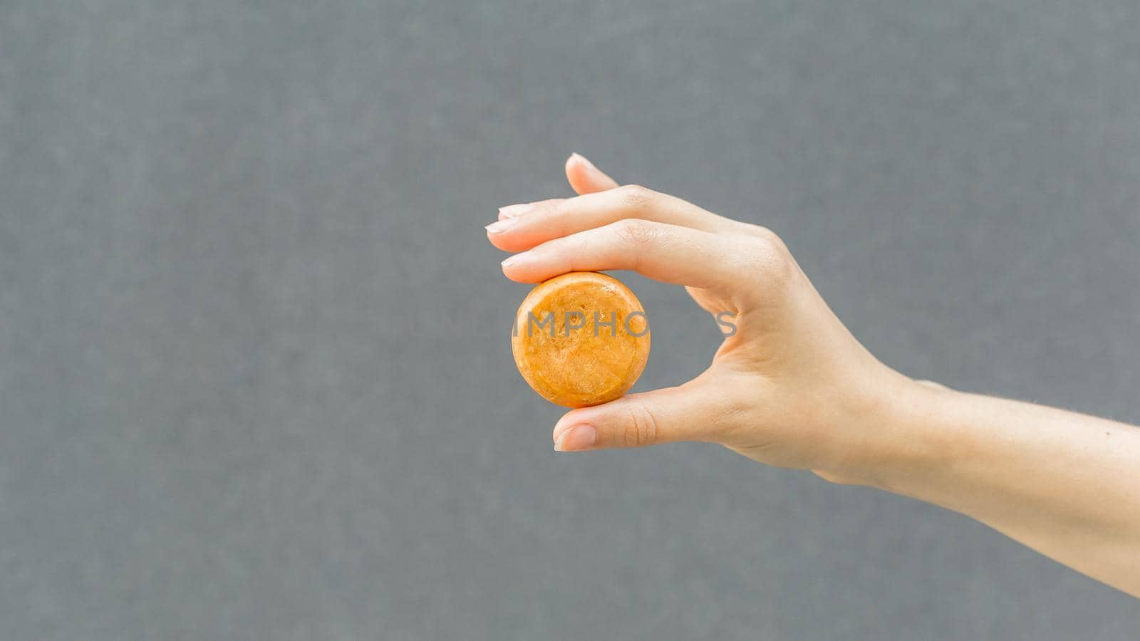 Woman hands holding organic soap or solid shampoo with no packaging over gray background. Healthy lifestyle, beauty, skin care, Zero waste concept. Copy Space for text