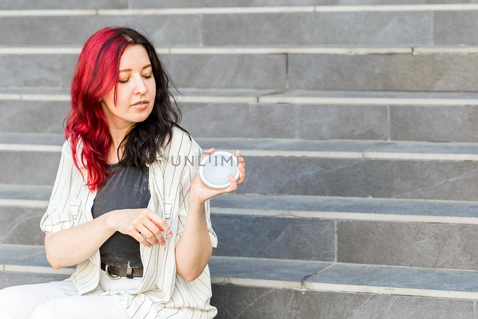 Young woman sitting on the stairs outdoors holding a silicone collapsible cup, reusable coffee-to-go tumbler.