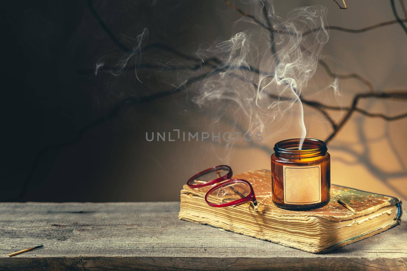 Vintage background with an old antique book, glasses and recently blown candle at night. Tree brunches and shadows make spooky dark academia mood. Cozy fall season reading time