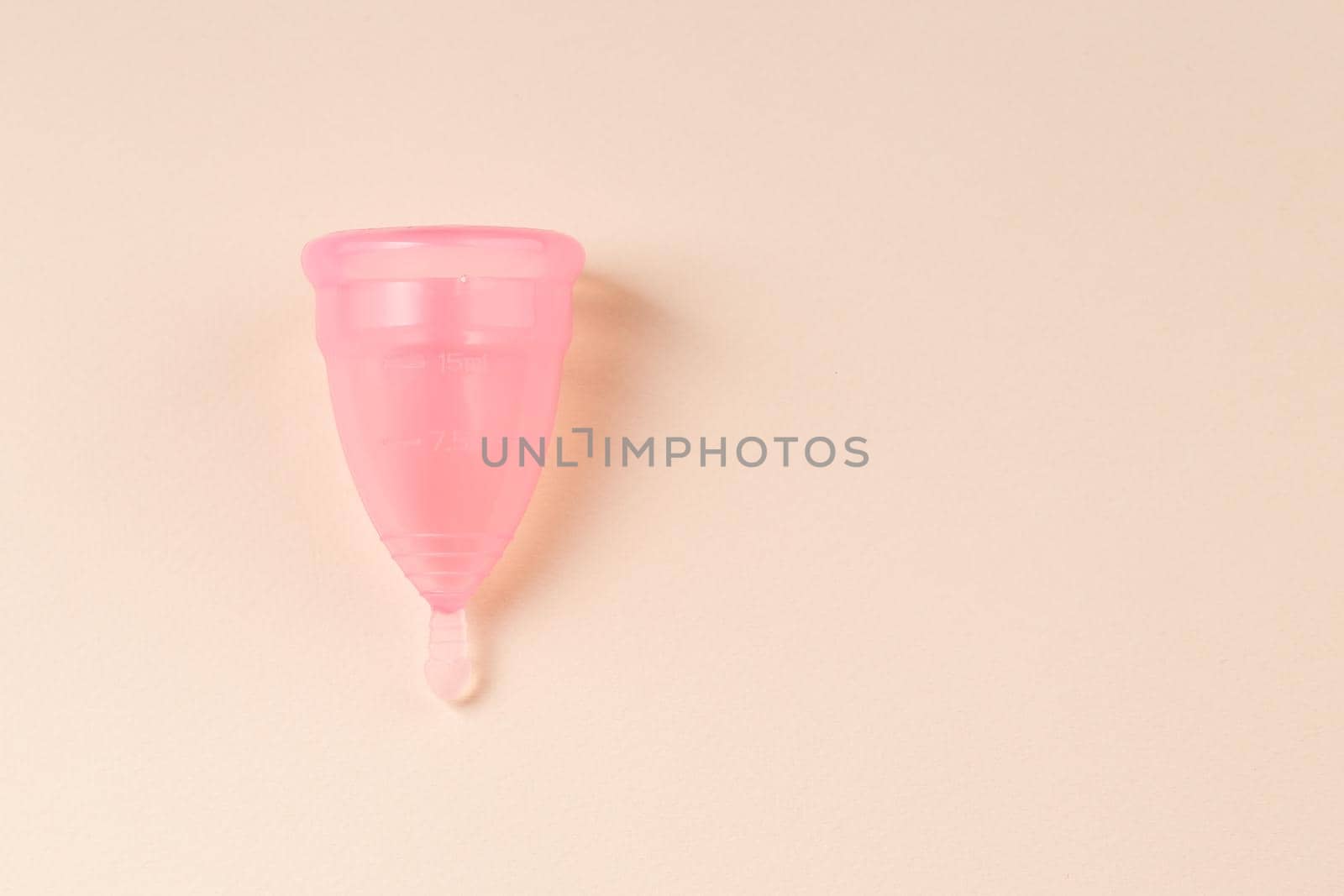 Pink Menstrual cup on bright beige background. Alternative eco friendly feminine hygiene product. Copy space.
