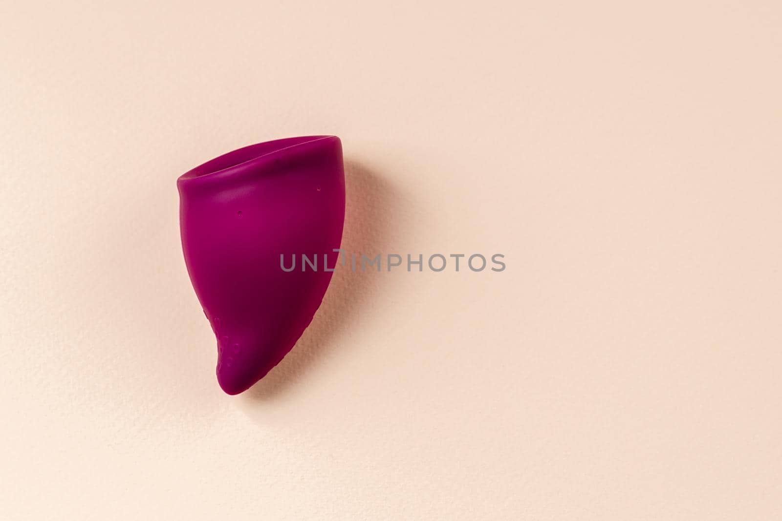 Bag shaped Menstrual cup on beige background. Purple silicone feminine hygiene product