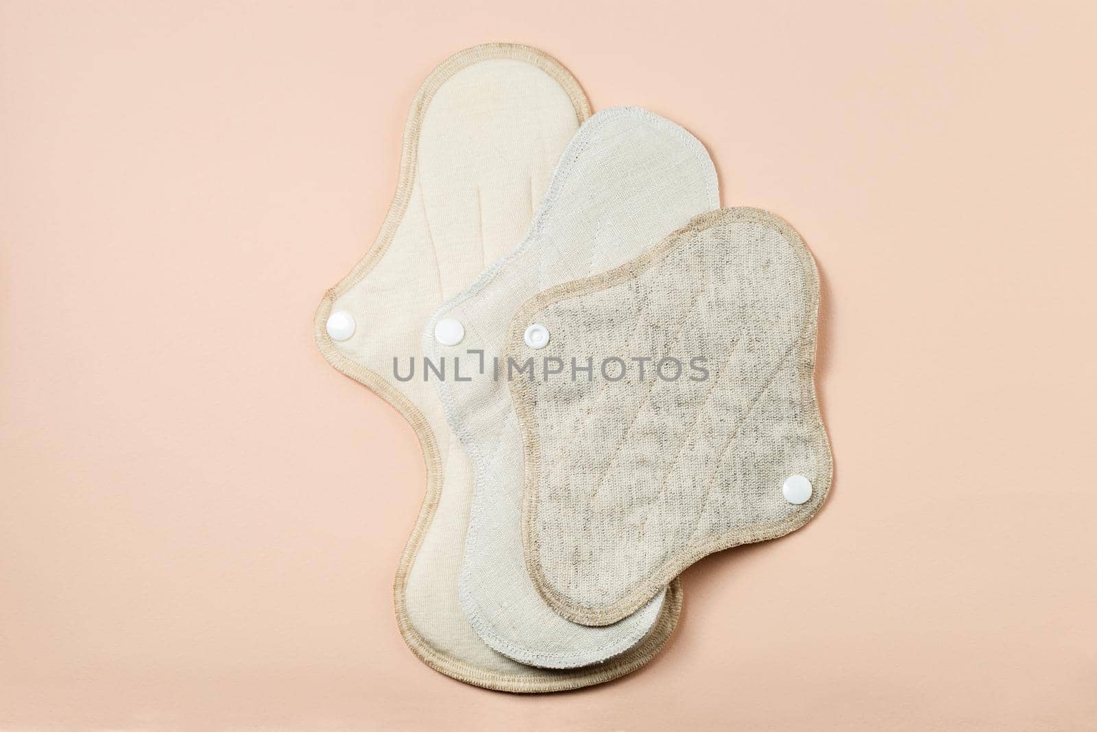 Reusable zero waste menstrual pads of differens size and textile on light beige background