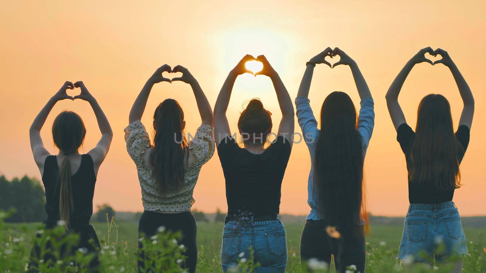 Five girls make a heart shape from their hands at sunset