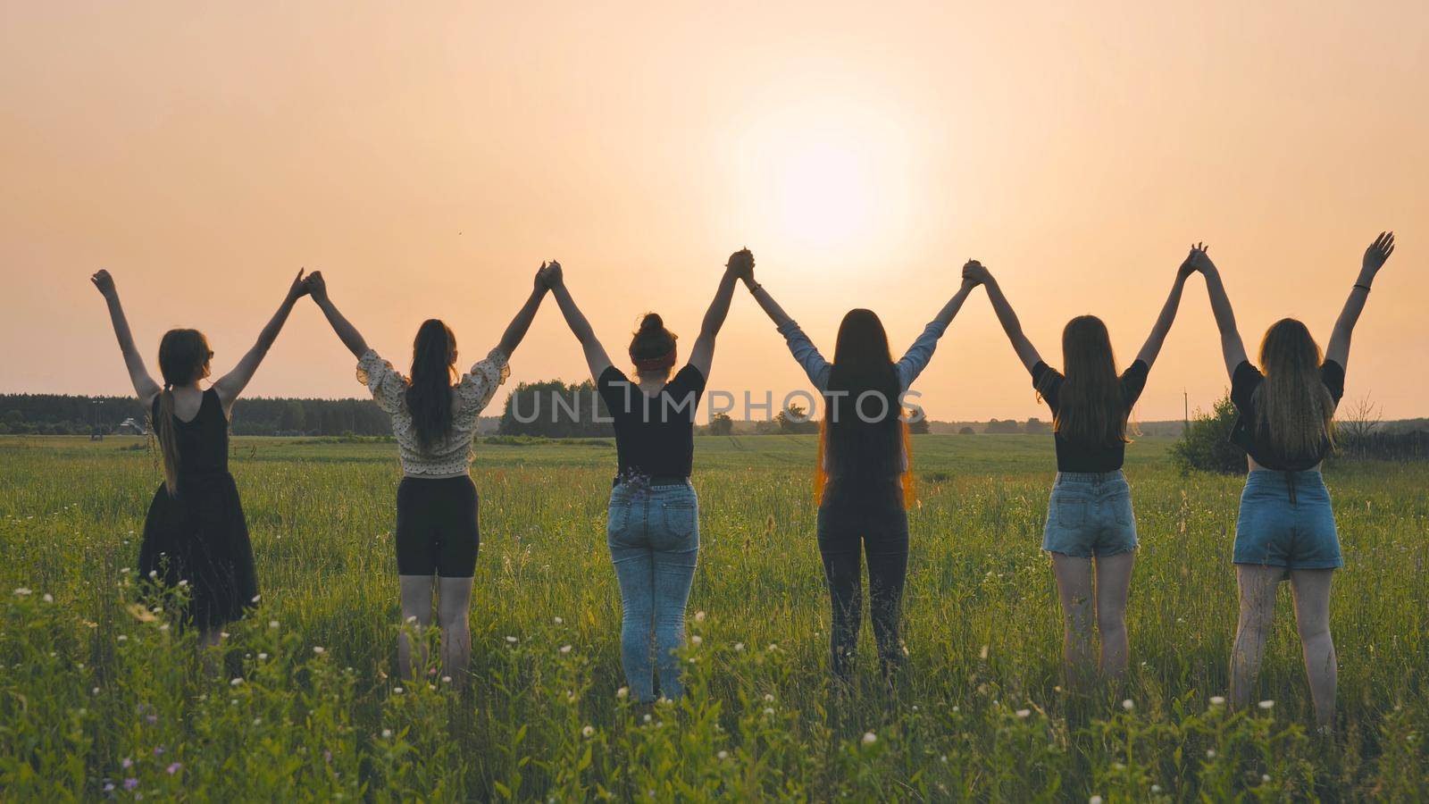 Girls friends raise their hands at sunset