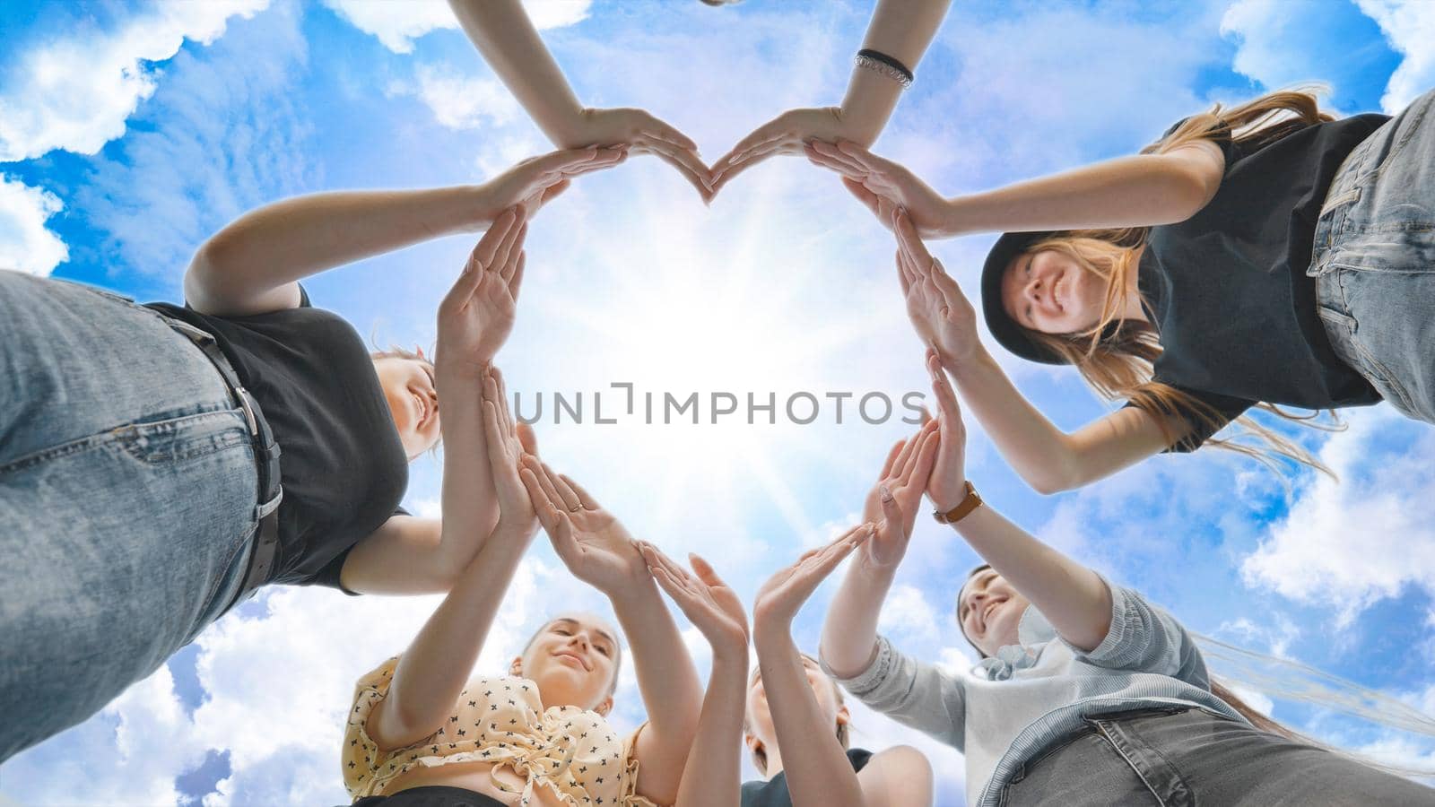 Girlfriends girls make a heart shape from their hands against the blue sky. by DovidPro