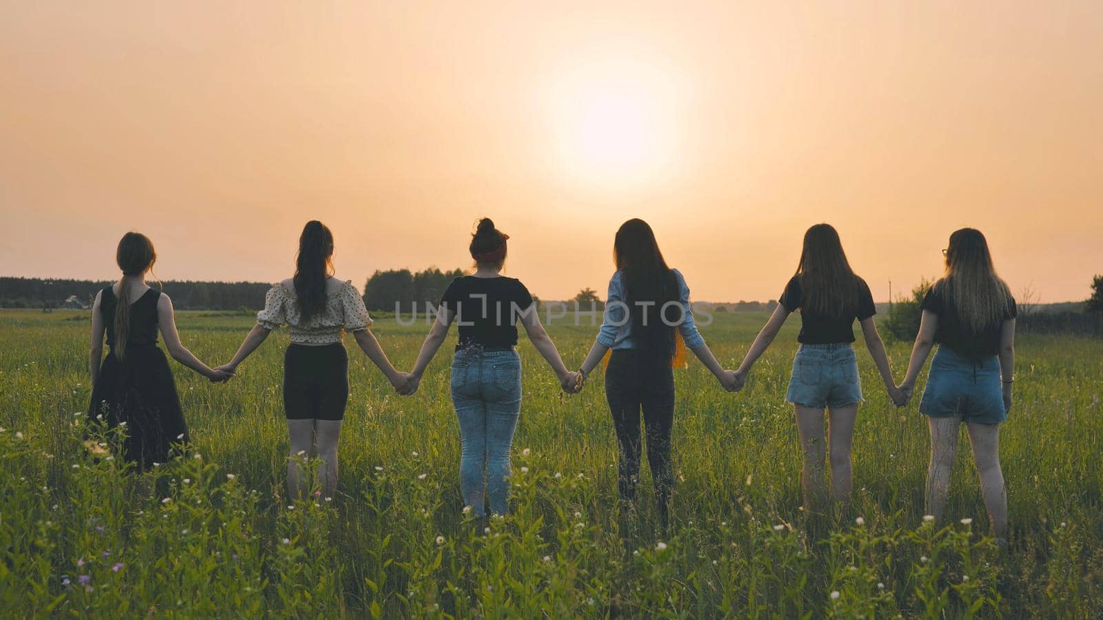 Girls stand holding hands at sunset on a summer evening. by DovidPro