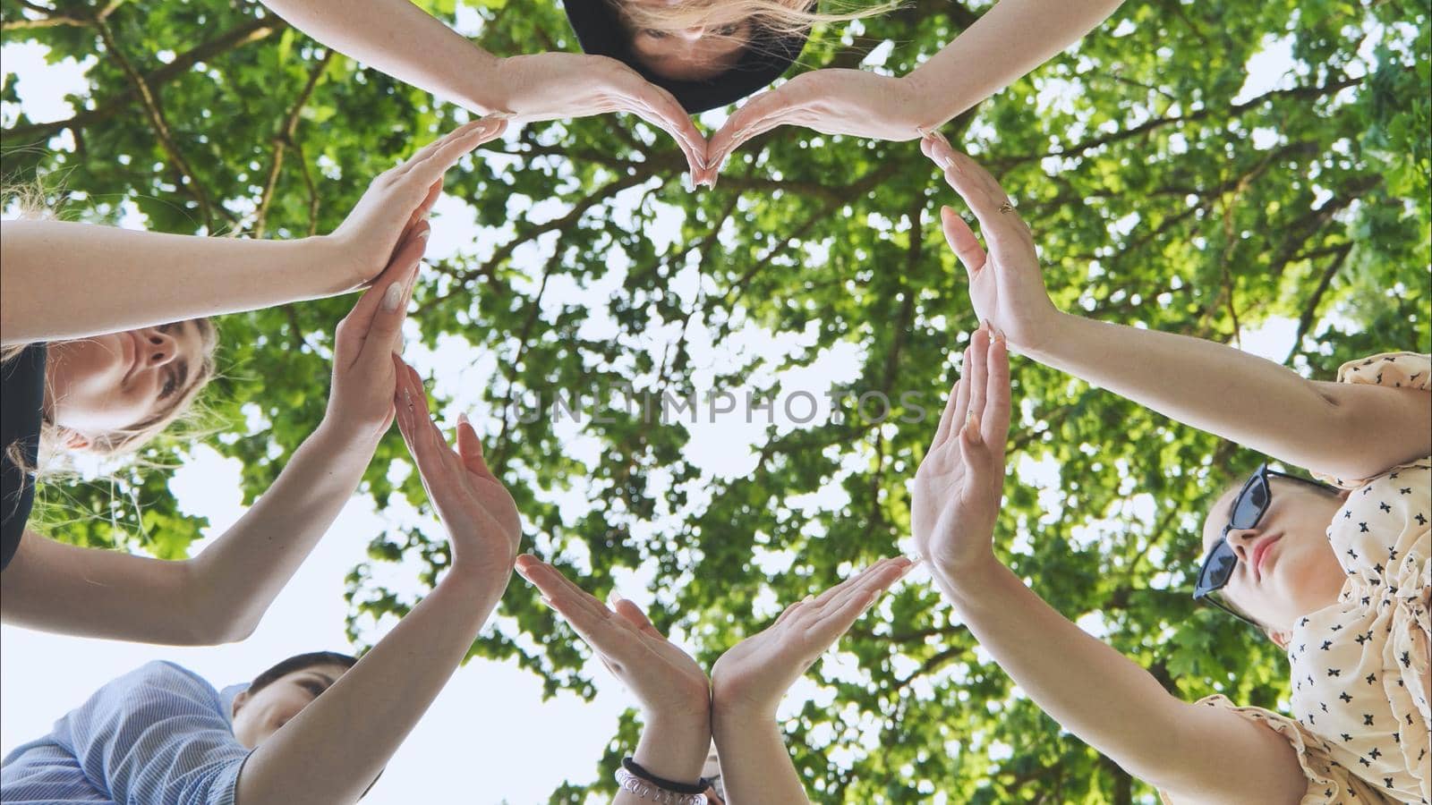 A group of girls makes a heart shape from their hands against the background of tree branches