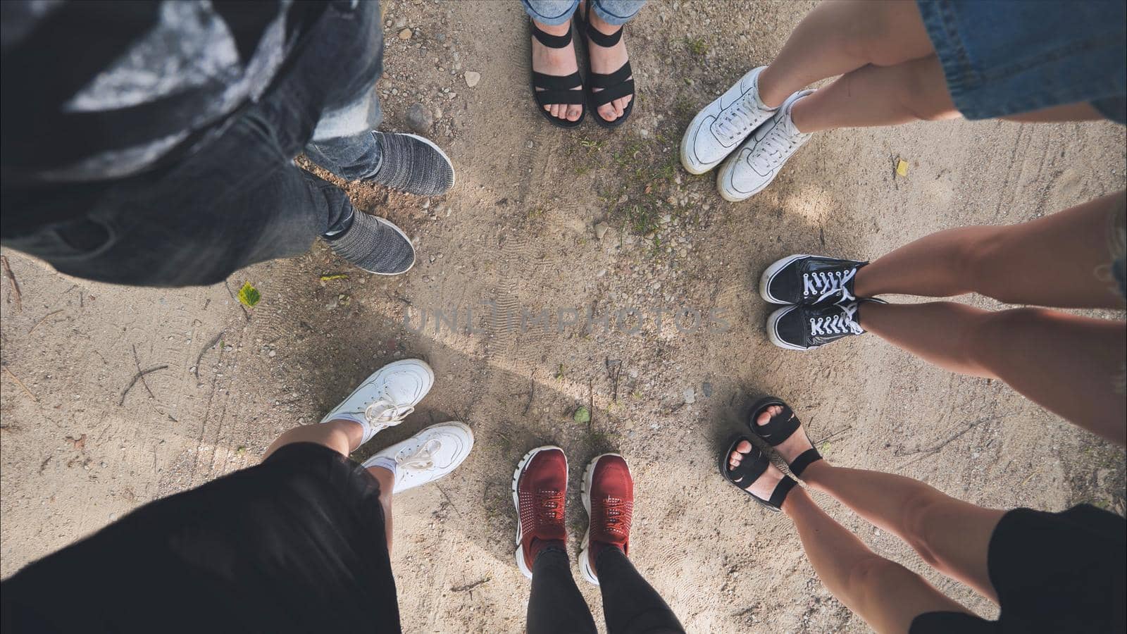 Legs and sneakers of teenage boys and girls standing in half circle on the sand. by DovidPro