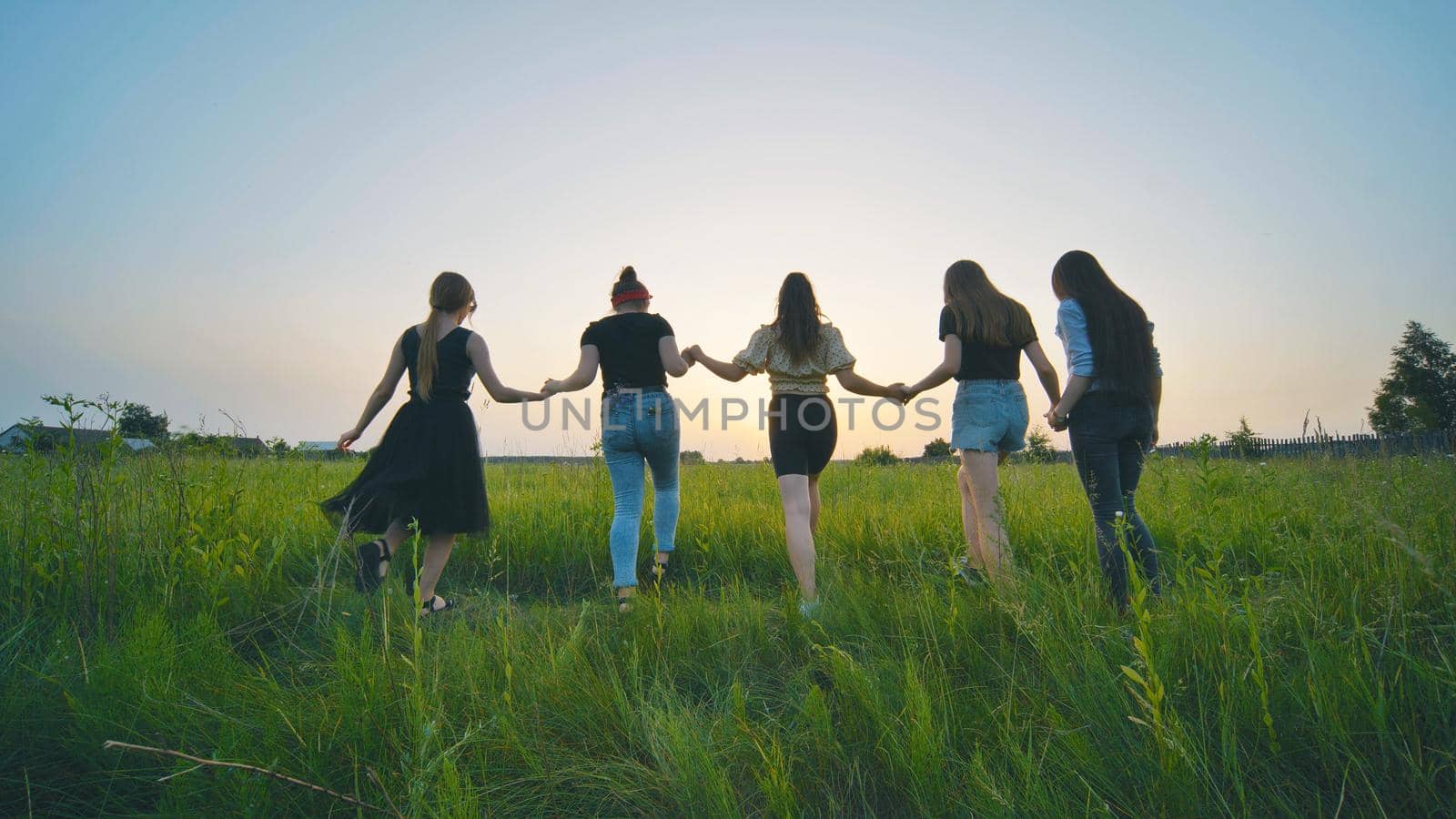 Girls friends go hand in hand at sunset across the field