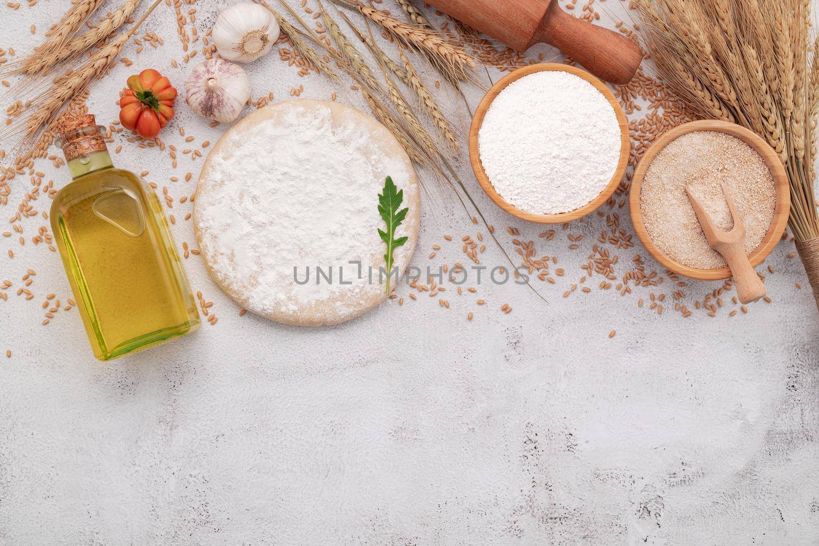 The ingredients for homemade pizza dough with wheat ears ,wheat flour and wheat grains set up on white concrete background.