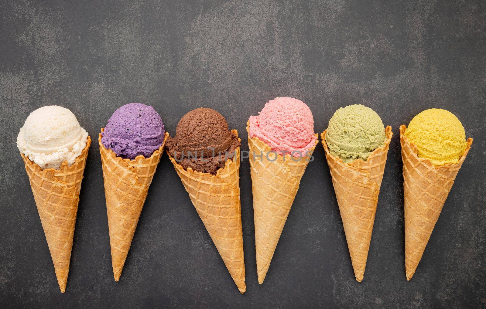 Various of ice cream flavor in cones blueberry ,pistachio ,almond ,orange and chocolate setup on dark stone background . Summer and Sweet menu concept.  by kerdkanno