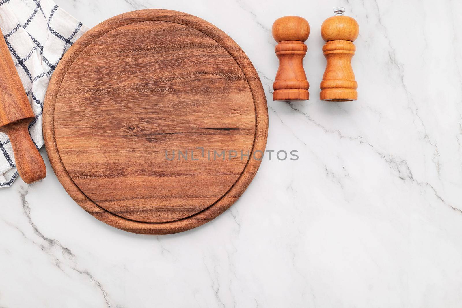 Empty wooden pizza platter with napkin and rolling pin set up on marble stone kitchen table. Pizza board and tablecloth on white marble background.